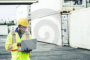 Black African worker working in logistic shipping using laptop to control loading containers at port cargo for import export goods