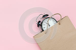 Black alarm clock in craft package on a pink background. Concept Black friday , season sales time. Flat lay Top view Copy space