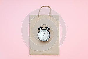 Black alarm clock on craft package on a pink background. Concept Black friday , season sales time. Flat lay Top view Copy space