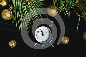 Black Alarm clock and fir tree branch, gold christmas decorations green velours glitte, shine background. Eve Time Concept on tabl