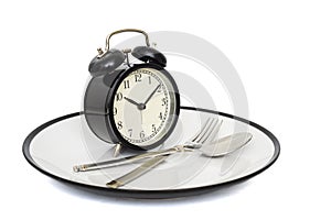 Black alarm clock with fork and knife on the plate. Isolated on white. Time to eat. Weight loss or diet concept