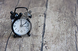 Black alarm clock isolated on wooden desk. The clock set at 2 o'clock. Conceptual photo