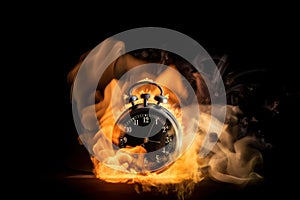 A black alarm clock with large numbers on a dark background surrounded by burning hot particles