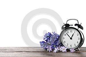 Black alarm clock and spring flowers on table against white background, space for text. Time change