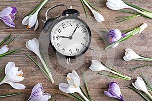 Black alarm clock and spring flowers on table, flat lay. Time change