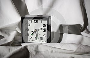 Black alarm clock on a white sheet with hard shadows