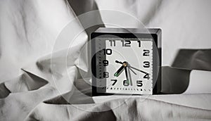 Black alarm clock on a white sheet with hard shadows