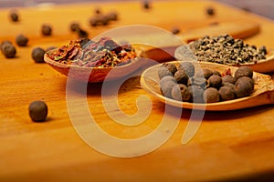Black allspice, coarse salt and various ground spices in wooden spoons on a wooden Board. Close up