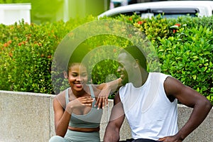 A black American man and woman couples resting after exercising in the garden chatting and smiling cheerfully at each other