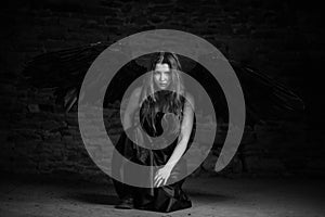 Black angel with red hair in a dark room. Dark stone background. Black and white image