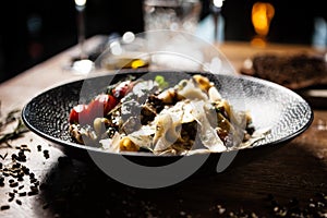 Black Angus pappardelle pasta with beef, champignon and parmegano cheese on a black plate. Delicious healthy