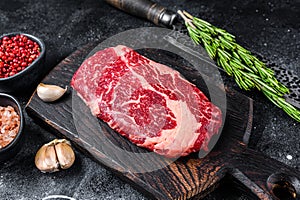 Black angus ribeye, raw rib-eye beef steak on a wooden board with knife. Black background. Top view