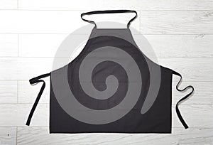 Black apron for kitchen top view on white wooden background.