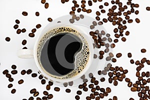 Black aromatic coffee with froth in a white mug among coffee beans in defocusing on a white background. View from above