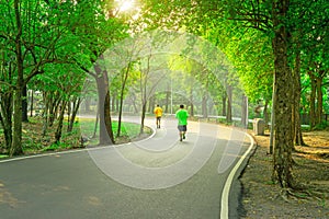 A black asfalt concrete jogging track in a public park, two people wearing yellow and green T shirt running on curve shape way photo