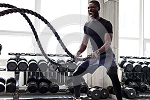 Black athlete doing battle rope exercise at crossfit gym