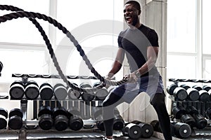 Black athlete doing battle rope exercise at crossfit gym photo