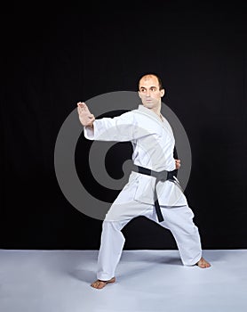 On a black background, an athlete in karategi trains a block with his hand