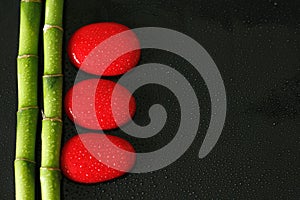 Black background with bamboo branch on the left and red zen pebbles with drops of water