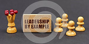 On a black background, chess and a sign with the inscription - LEADERSHIP BY EXAMPLE