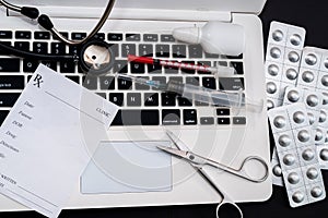 white laptop on which a stethoscope, pills, syringe, thermometer and a side notebook with a pen