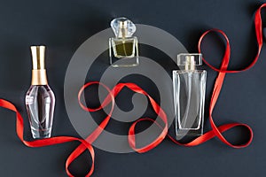 on a black background, a red satin ribbon and three bottles of women's perfume. layout.