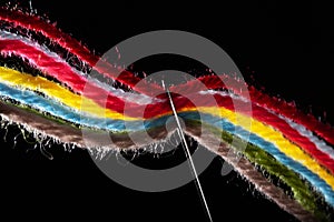 On a black background, several bright multicolored woolen threads are pass through the eye of the needle. Close-up. Backlight