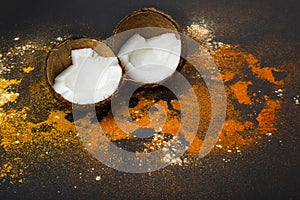 On a black background, a split coconut around which spices are scattered.