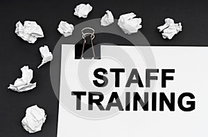 On a black background, there are crumpled pieces of paper and paper with the inscription - Staff Training