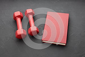 On a black background two red dumbbells and one red book. symbols of knowledge and power