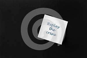 On a black background, a white sticker with the inscription: `Replay the crisis`