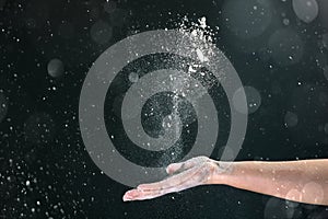 On a black background, a woman`s hand pours white flour like snow for baking