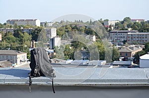 Black backpack lies on metal border of residental multistorey building rooftop in sunny weather