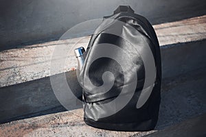 Black backpack with reusable steel thermo water bottle inside on urban stairs.
