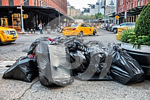 Black bags of trash on sidewalk in New York City street waiting for service trash truck. Garbage packed in big trash bags ready