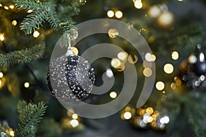 Black ball on a Christmas tree against the background of a golden garland.