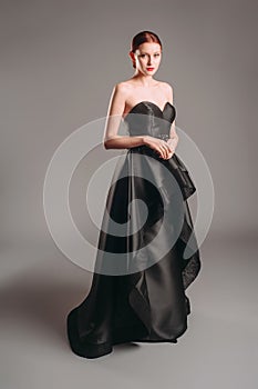 Black ball gown. Attractive ginger young woman in sleeveless evening dress on studio background. Holiday outfit. A line timeless d photo