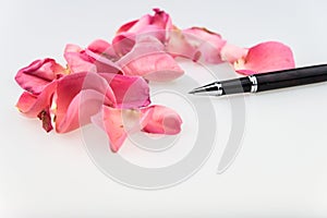 Black Ball Point Pen with light pink rose petal on white background