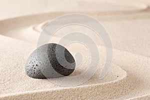 Black basalt stone on sandy beach sand with line pattern