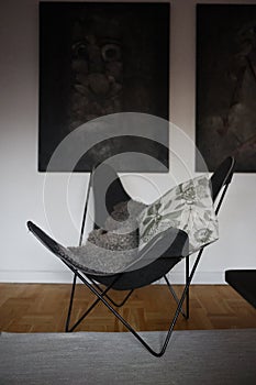 A black bat-wing armchair stands on the floor with two paintings behind.