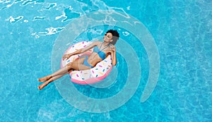 Black beach girl in sexy bikini floating on inflatable ring at swimming pool, empty space