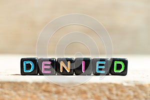 Black bead with letter in word denied on wood background