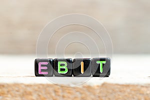 Black bead with letter in word EBIT Abbreviation of Earnings Before Interest and Taxes on wood background