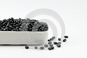 Black beans are housed in white ceramic vessels and placed on a white floor, selective focus, space for text