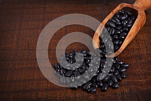 Black beans in scoop on wooden background