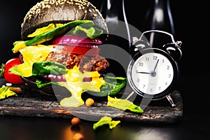 Close-up of black beef burger with flowing melted cheese and clock on a black background.