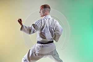 A black belt athlete performs formal exercises against a colored background with yellow and green tints