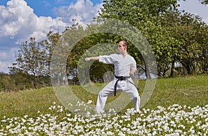 With a black belt, an athlete strikes with a hand while standing on the green grass