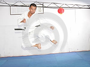 Black belt karate man jumping to give a high kick