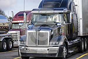 Black big rig modern semi truck with semi trailer standing on truck stop with another semi trucks